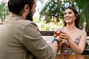 romantic man giving present to pretty woman in table outside