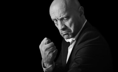 Serious man shows a fig, insulting hand gesture, black and white photo. Black and white portrait, brutal man gesturing no.