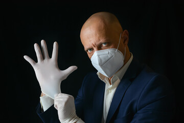 An elegant man in a medical mask puts rubber gloves on his hands. An elegant man in a business suit...