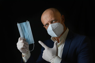 An elegant man in a business suit demonstrates the means of protection against viral infections and respiratory infections, black background. A man holds medical masks in his hands.