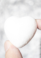 Creative Valentines Day love minimal composition made of man's fingers holding white heart on sparkling silver blurred background. Aesthetic artistic.