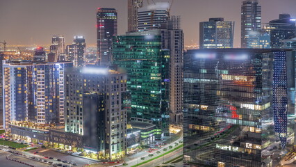 Business Bay Dubai skyscrapers with city lights reflected on glass aerial night timelapse.