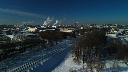 Industrial area on the outskirts of the city. Factory buildings are covered with snow. Factory pipes are visible. Winter industrial landscape. Aerial photography.