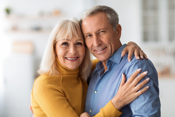 Loving Mature Spouses Embracing Smiling Standing In Kitchen At Home