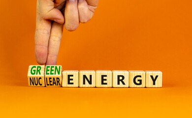 Nuclear or green energy symbol. Businessman turns wooden cubes and changes concept words nuclear energy to green energy. Beautiful orange background copy space. Business nuclear green energy concept.