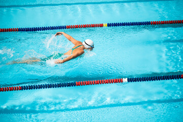 Wide shot of a Caucasian female athlete doing the butterfly stroke to swim the pool. © TheSupporter