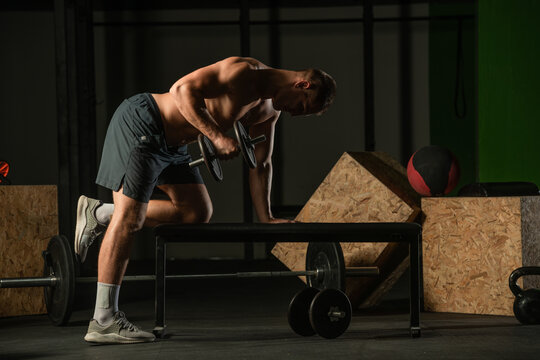 Athletic caucasian man doing a dumbbell triceps kickback with his right arm on a horizontal bench.