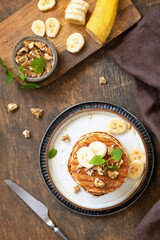 Celebrating Pancake day, american breakfast. Delicious homemade banana pancakes with nuts and caramel on rustic wooden table. Top view flat lay.