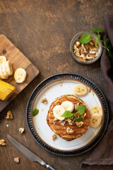 Celebrating Pancake day, american breakfast. Delicious homemade banana pancakes with nuts and caramel on rustic wooden table. Top view flat lay. Copy space.