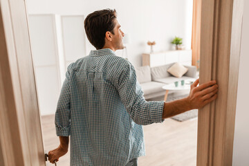 Back view of excited young man walking in apartment