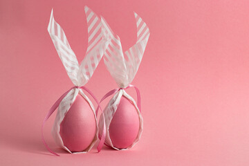 Two pink eggs wrapped in paper in the form of an Easter bunny on a pink background. Preparation for Easter. Copy space