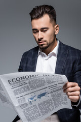 bearded businessman in plaid blazer reading newspaper with economic news isolated on grey.