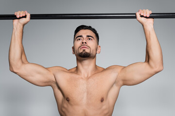 muscular young sportsman exercising on horizontal bar isolated on grey.