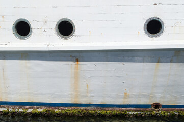Detail of an old abandoned rusted ship, part of hull plating and round windows with an old peeled...