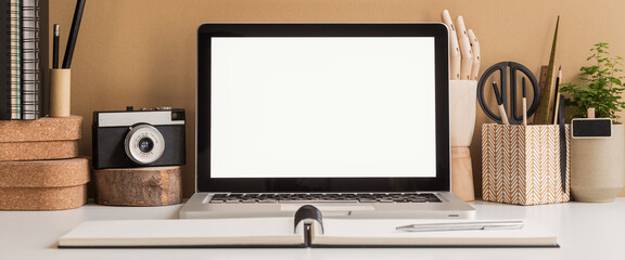 Creative desk with a laptop screen frame, desk objects, office supplies, books, and plant on a brown background.	
