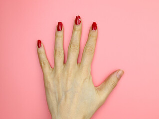 Peeling nail polish. Girl's hand with red nail polish without manicure top view. Not well-groomed hands on a pink background.
