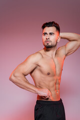 red lighting on shirtless sportsman posing while showing muscles on grey and pink.