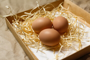 Closeup rustic eggs in box on craft background. Easter craft box with brown eggs on eco background. Chicken eggs on craft table with hay and straw. Close-up view of raw product. Wooden straw
