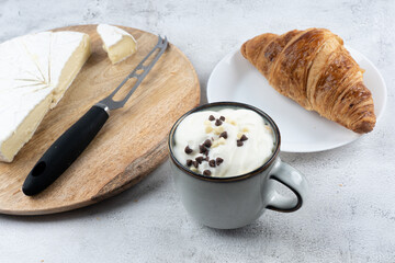 A cup of coffee, Butter bun, cheese knife and sliced round white cheese - on a wooden board plate. HOME breakfast
