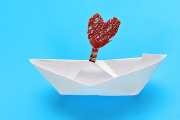 white paper boat with a red heart on a blue background