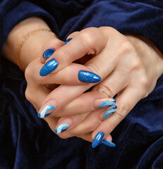 Female hands with a multicolored manicure on dark blue background closeup