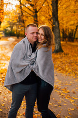 Young couple is walking in the sunny autumn park. Happy boy and girl are rolling themselves in the rug near yellow tree. Fallen yellow leaves, brith warm autumn weather. Autumn love story in park
