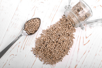 dried white pepper in a spoon and poured out of a jar on a white wooden background