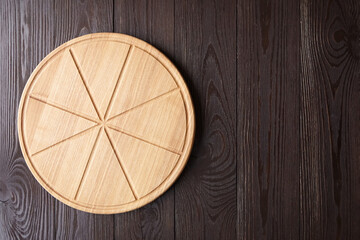 Round pizza cutting board with slice grooves on wooden table top view