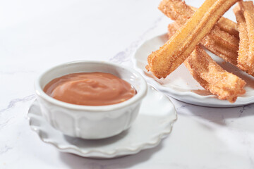 Traditional churros with sugar and cinnamon served on a marble table, with a bowl of caramel...