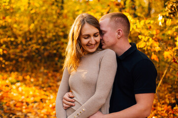 Fototapeta premium Young couple is having a walk in the sunny autumn park, forest. Happy man and his woman are hugging . Fallen yellow leaves, brith warm autumn weather. Autumn love story in park 
