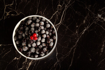 Top view of a handful of ripe blueberries in a white cup on a dark background