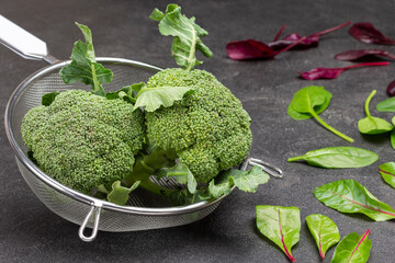 Broccoli cabbage in colander. Spinach leaves on the table.
