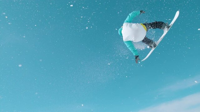 SLOW MOTION, LENS FLARE: Snowboarder does a spectacular spinning grab trick while riding in a snowpark. Athletic male tourist takes off a large kicker and does a 360 grab while flying through the air.