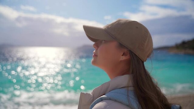 Close-up shot of a young woman against the background of a shining sea. A girl enjoys a sunny day on the beach on a trip