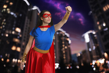 Confident young woman wearing superhero costume and beautiful cityscape in night on background