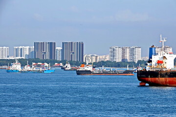 Various types of sea vessels and tugboats on the background of the coastline and city line of the city of Singapore.