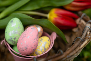 Obraz na płótnie Canvas Scena con un cesto con tulipani rossi e un secchiello pieno di uova di pasqua colorate in primavera ad aprile. Vacanze. Feste di primavera. Celebrazione.