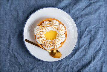Lemon tart decorated with wiped cream. Decorated with flowers and different cloths and golden spoon. Lemon custard cream and sweet dough.