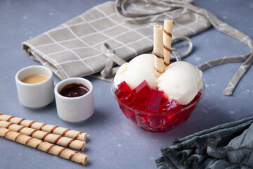 A tasty ice cream with ref jelly, chocolate and caramel on a gray table
