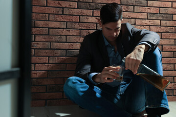 Addicted man with alcoholic drink near red brick wall