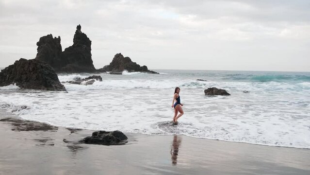 Beautiful woman in swimming suit walking on a black sandy beach in the Canary Islands, Tenerife