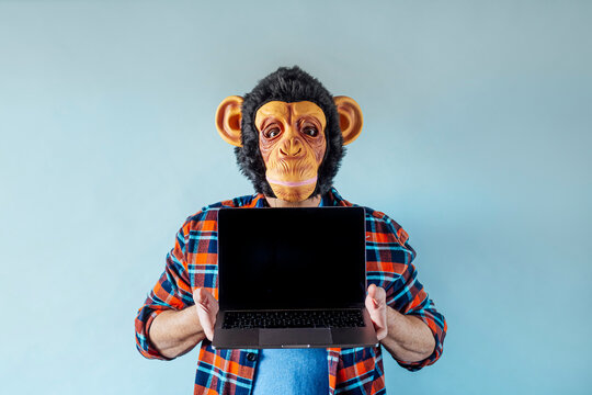 Man wearing monkey mask and using a laptop.