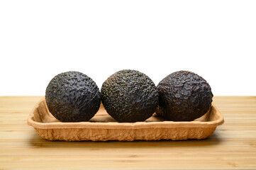 Three black avocados in a package on a wooden table. Isolated white background.