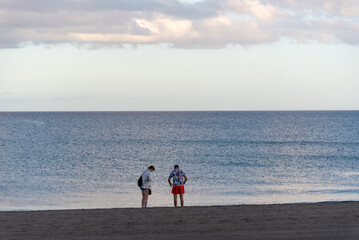 Pareja de jóvenes de espaldas en un atardecer en la playa con el mar en calma y el cielo despejado en un día de verano en Lanzarote, Islas Canarias.