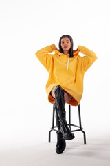 Attractive woman of Latin appearance wears a yellow hoodie on a white background. The girl looks sexy and happy. The elegant brunette is wearing a bright sweatshirt. All-season clothing