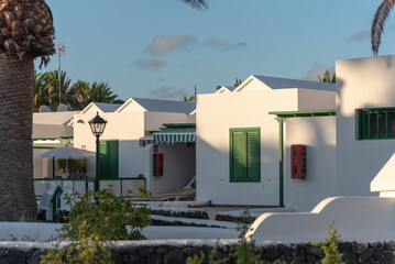 Fototapeta na wymiar Casas típicas de Lanzarote en Islas Canarias con fachadas de color blanco y toldos verdes coloridos rodeadas por palmeras un día soleado de verano con el cielo azul despejado