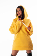 Attractive woman of Latin appearance wears a yellow hoodie on a white background. The girl looks sexy and happy. The elegant brunette is wearing a bright sweatshirt. All-season clothing