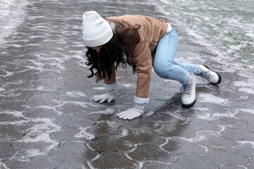 Young woman trying to stand up after falling on slippery icy pavement outdoors