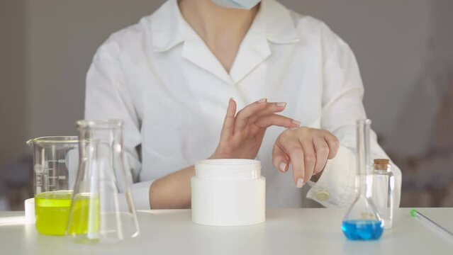 Scientist or pharmacist applying moisturizer lotion on her hand for efficacy testing of natural organic skincare products in laboratory.