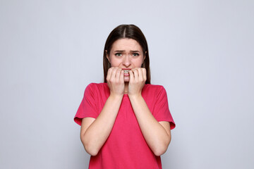Young woman biting her nails on light grey background